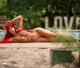 Harley Cameron stretched out sexily on the pool edge in a daring leopard-print chain monokini, one hand in her red hair, her perfect body and curves on full display in this hot Fitness Gurls shoot.