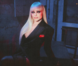 Close-up portrait of Liv Morgan with platinum blonde hair illuminated by blue light, wearing a black blazer with a red "Liv Morgan" patch for PAPER Magazine.