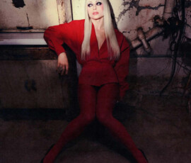 Liv Morgan sits on the floor in a derelict industrial setting, wearing a striking red blazer, bodysuit, and red tights with black heels for PAPER Magazine.